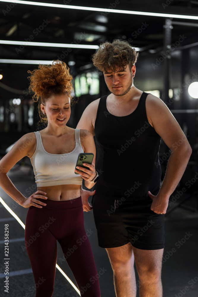 Naklejka premium Young couple using smartphone in modern gym