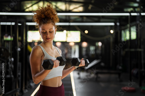 Young woman lifting dumbbells performing bicep curls in gym