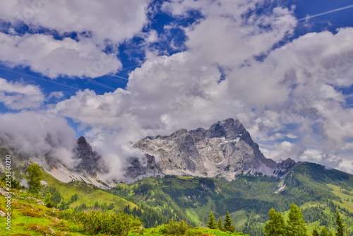 Panoramic alpine landscape around Salzburg, Austria, featuring majestic snow-covered peaks, rugged mountain ridges, green foothills, forested slopes, and picturesque valleys of Austria
