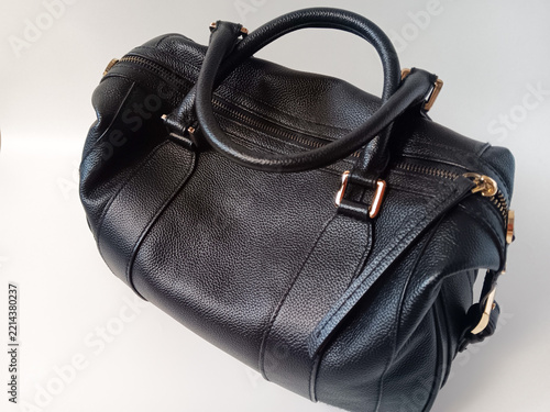 Close up of black leather woman handbag with a round top handle, zip top and gold hardware isolated on a white background.