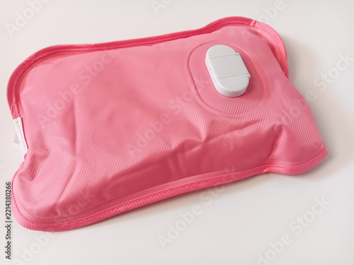 Close up of a pink rechargeable electric hot water bag (or electric heating pad) with a soft-touch ribbed PVC surface and a central charging port cover, used for soothing warmth and muscle relief isol