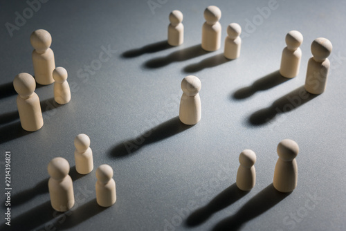 A lone wooden figure surrounded by groups of people, representing loneliness in a crowd, social disconnection, isolation and lack of meaningful human connection despite being around others