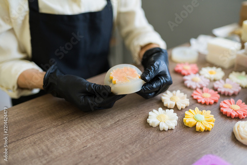 Closeup of a woman wearing gloves demolding handmade flower soap from a silicone mold during artisan crafting process