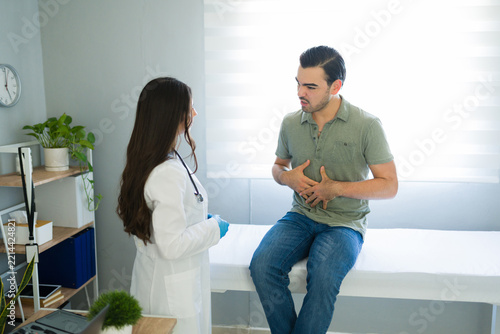 Patient suffering from stomach ache and abdominal pain consulting female doctor for medical diagnosis in office