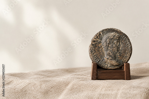 Weathered antique coin on wooden stand over linen fabric, history and heritage concept