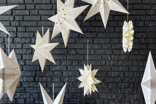 White paper star decorations hanging in front of a dark brick wall background for holiday interior decor