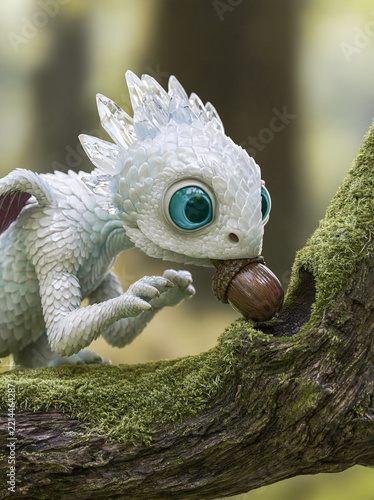 Tiny white fantasy dragon holding an acorn while perched on a mossy tree branch in woodland scenery