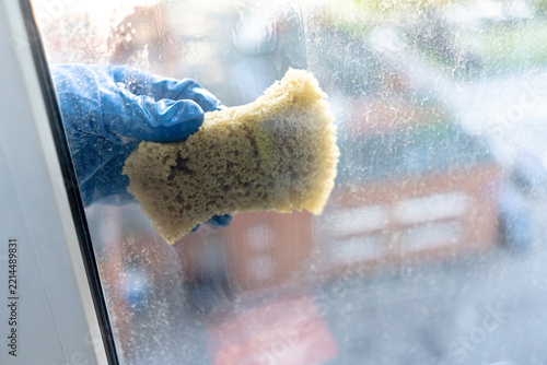 Obraz na plátně Blue gloved hand scrubbing a wet glass window with sponge