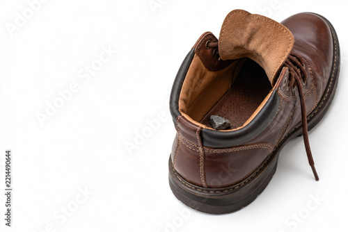 Small dark stone lies inside an open brown leather boot. Space for text.