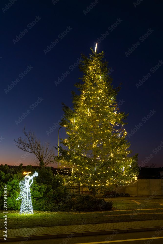 Fototapeta premium Chvalovice Christmas tree and angel illuminating holiday evening