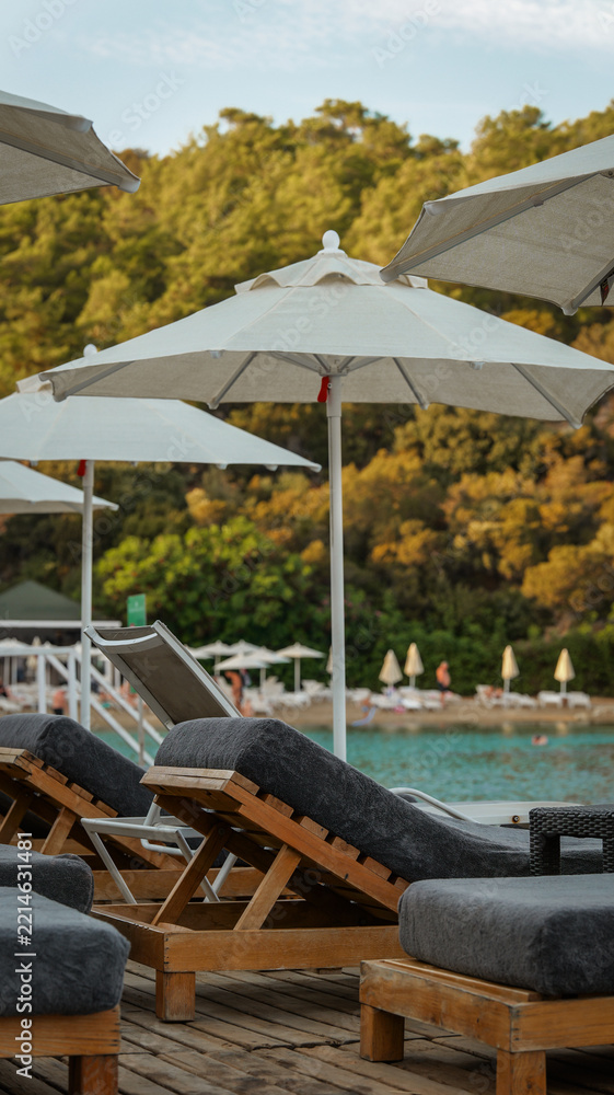 Fototapeta premium Sun loungers with white umbrellas on a wooden deck overlooking a serene turquoise sea bay