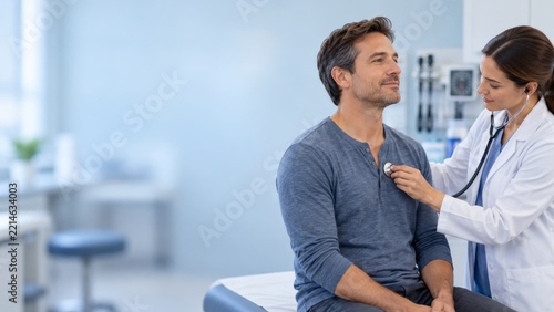 Doctor Listening to a Seated Man with a Stethoscope in a Blue Clinic