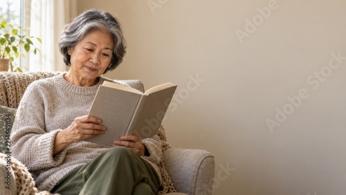Senior woman reading a book in an armchair beside a bright window