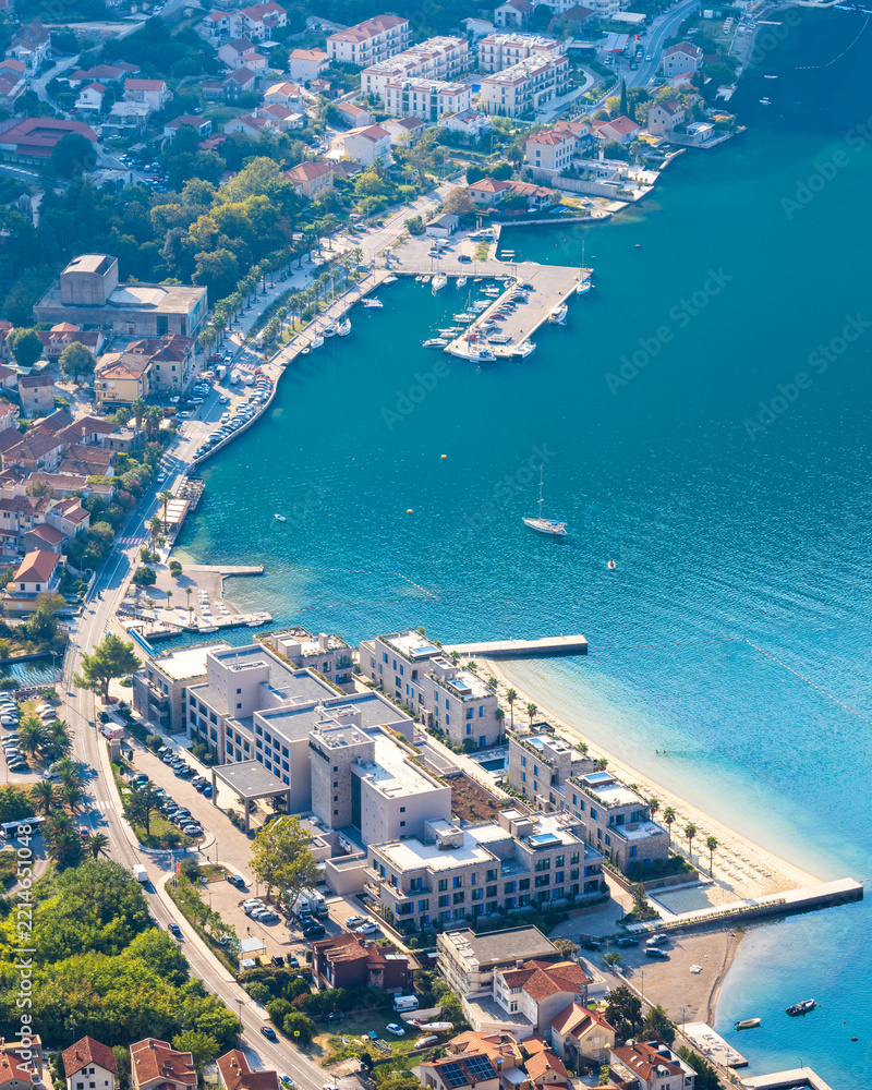 Fototapeta premium Aerial high-angle view of Risan town in Kotor Bay, Montenegro in soft early morning light, featuring coastal architecture, harbor, and calm blue Adriatic sea.