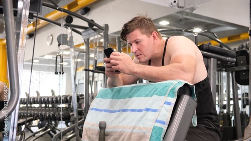 Muscular man resting on a preacher bench between sets in a modern gym, concept of workout recovery, fatigue, bodybuilding, strength training, sports performance, discipline and fitness lifestyle.