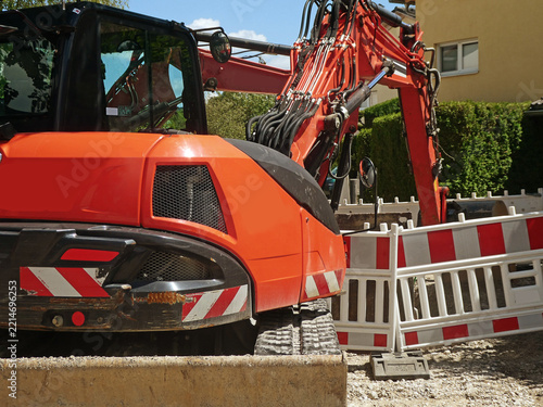 Germany, Bavaria, Garching near Munich - Bulldozer with shovel in pause  to repave the road with a white and red safety barrier around the street work