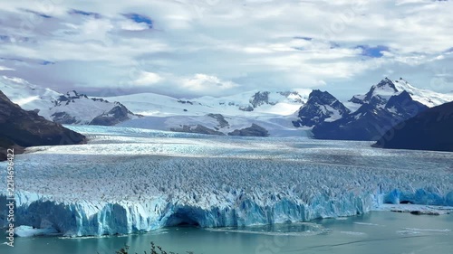 Scenic aerial drone footage of the magnificent Perito Moreno Glacier in Argentina, showcasing majestic ice formations, snowy mountains, and tranquil turquoise water under a dramati