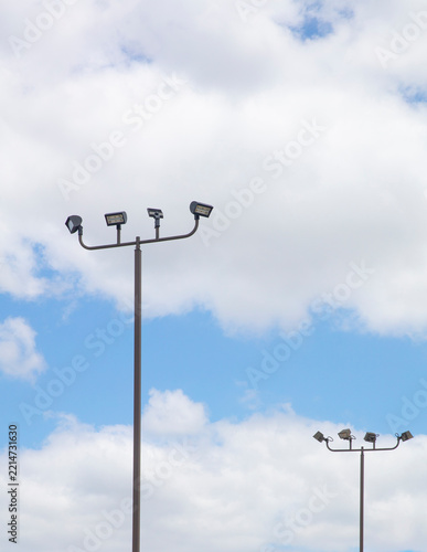 Outdoor commercial LED parking lot light pole with multiple LED flooding and bullhorn brake agains and blue and cloudy sky.  Vertical frame
