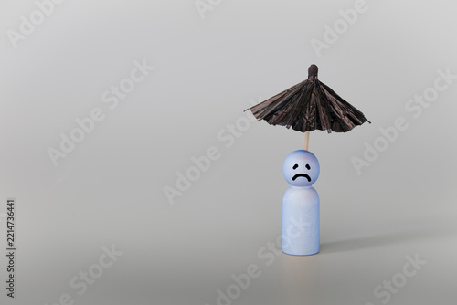 Psychology, solitude, fear or mental health problem concept. Depressed sad person with a cloud overhead, on grey background. Wooden figure with black umbrella symbolize mental health.
