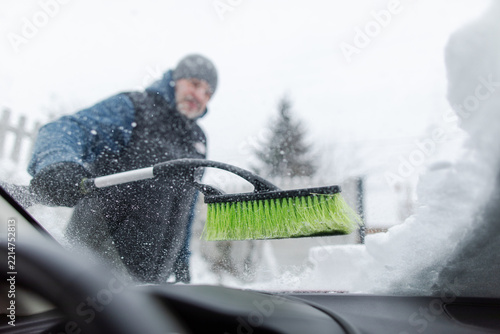 Man clearing fresh snow from windshield with brush, preparing vehicle for safe winter driving, view from inside vehicle
