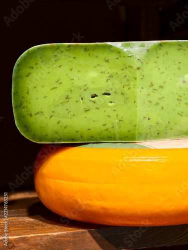 Obraz na plátně Green hard cheese wrapped in clear food film placed on a large round yellow chee