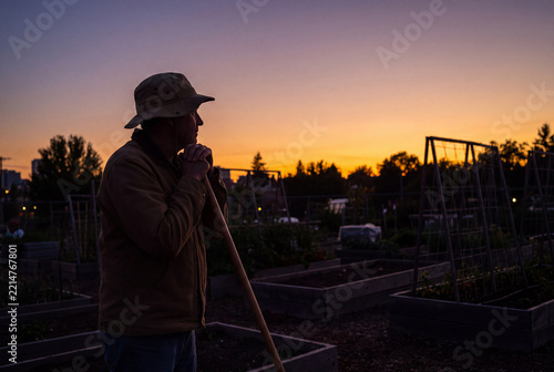 Silhouetted Gardener Resting on Tool in Community Garden at Sunset