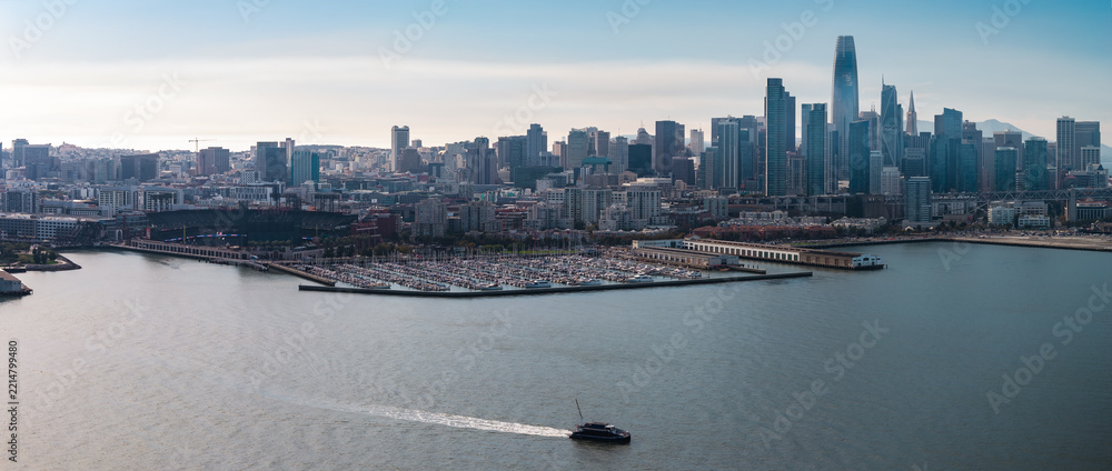 Fototapeta premium San Francisco skyline and South Beach Harbor are captured in an aerial view across the bay, showing skyscrapers like Salesforce Tower, Oracle Park stadium, and a small boat navigating open water.