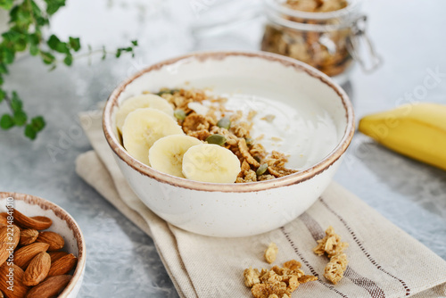 Greek yogurt with muesli and sliced banana in a bowl on a marble countertop