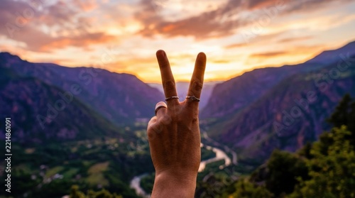Hand making peace sign against sunset mountain valley backdrop