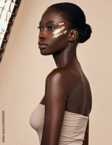 Beautiful young african woman with flawless dark skin wearing golden face paint in studio lighting
