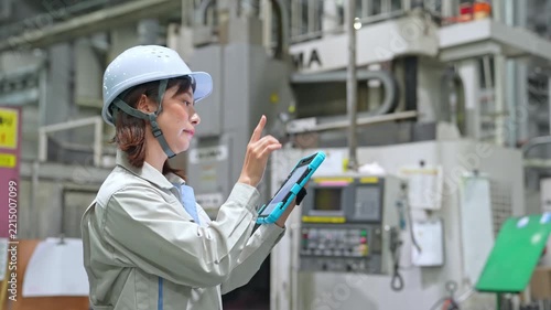 Female worker inspects factory machinery with a tablet.
