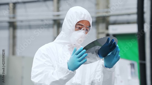 A male worker in protective clothing inspects silicon wafers at a semiconductor factory.