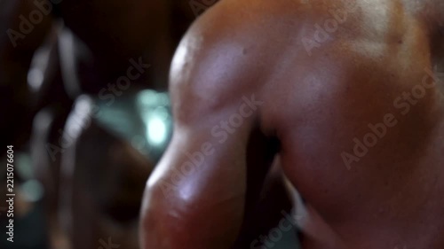 Muscular bodybuilder flexes oiled tanned arm bicep in dramatic studio lighting, showcasing fitness dedication, athletic definition, and intense physique power. 4K video.