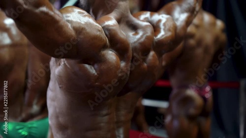 Muscular bodybuilder flexes defined back muscles, deltoids, and lats with competition tan under dramatic backstage lighting, showcasing peak athletic physique. 4K video.