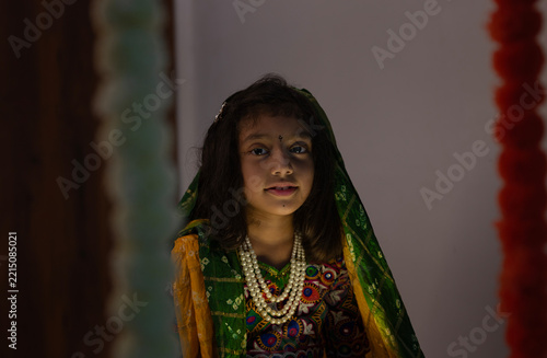 Portrait of a young Indian girl wearing traditional Gujarati ethnic clothing with a green patterned dupatta, colorful embroidered blouse, and layered pearl necklace.