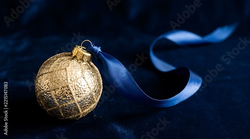 A single textured gold Christmas bauble with a blue ribbon on a dark navy velvet background