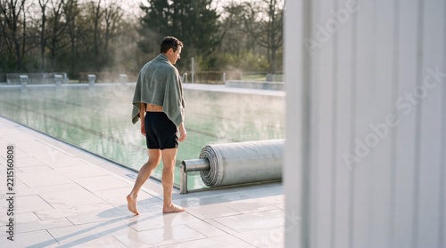 Man walking barefoot with towel beside outdoor pool cover