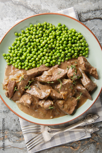 German baden beef liver with onions, braised in white wine and served with green peas close-up shot on a plate on a table. Vertical top view from above