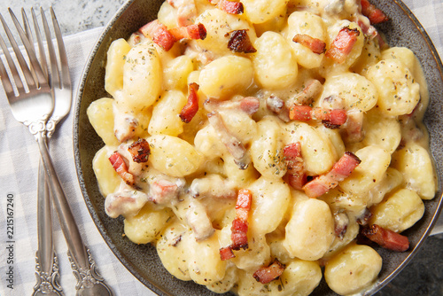 Close-up of potato gnocchi with fried bacon, velvet sauce, and Parmesan in a bowl on a table. Horizontal top view from above