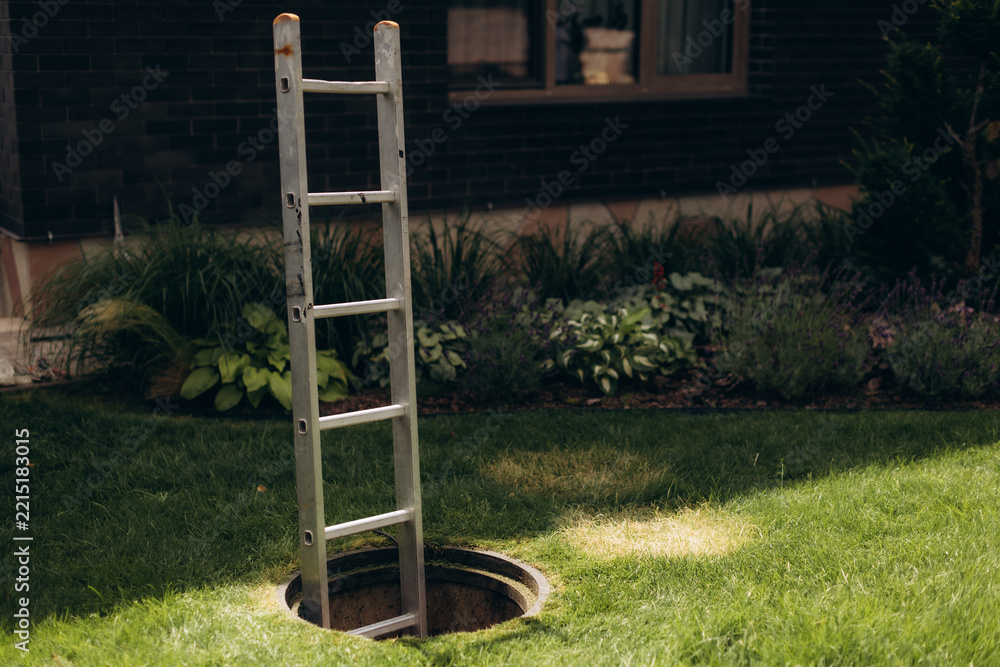 Naklejka premium Aluminum ladder entering open manhole on green lawn