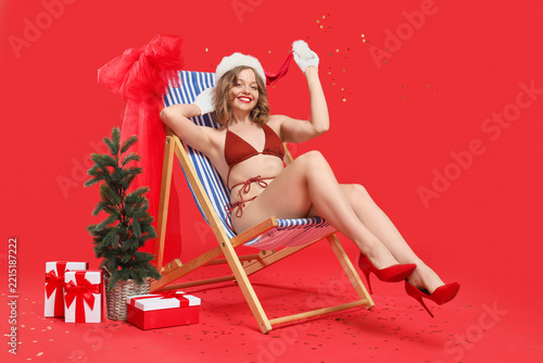 Attractive young woman in swimsuit with Christmas gifts on deck chair against...