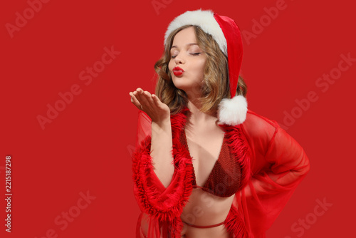 Attractive young woman in swimsuit with Santa hat blowing kiss on red backgro...