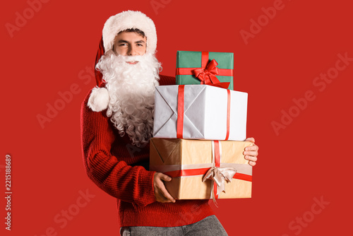 Young Santa Claus with Christmas presents on red background