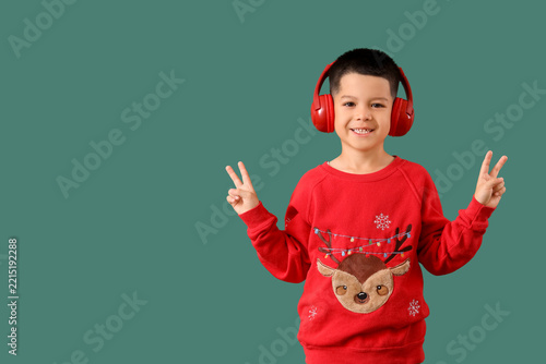 Cute happy little Asian boy in Christmas sweater and headphones showing victo...