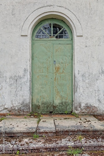 Arched doorway with a weathered green metal door set into a light-colored, textured plaster wall, Estonia, Europe.