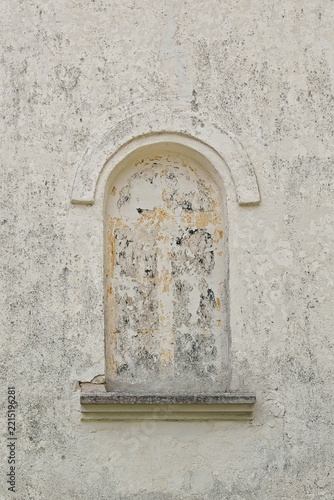 Arched, weathered wall niche or a blocked-up window with peeling plaster and faded remains of an old fresco or painting on a textured, off-white exterior wall, Estonia, Europe.