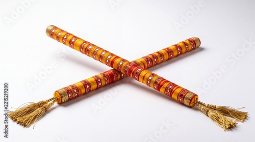 Authentic Gujarati dandiya sticks crossed on white surface, wrapped in saffron and crimson silk thread with mirror work and gold tassels
