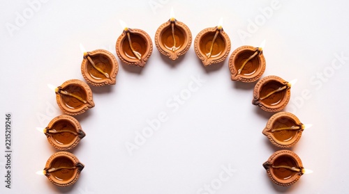 Semicircular arrangement of traditional clay diya oil lamps with glowing flames, flat lay on white background with copy space