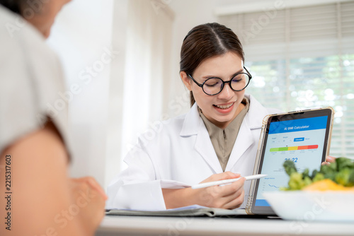 Asian woman nutritionist showing AI BMI calculator on tablet and explaining to senior patient, doctor using digital health technology for medical diagnosis, wellness planning and weight control.
