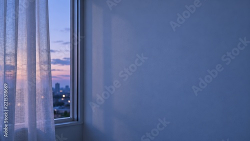 Sheer Curtain and Sunset City View Beside a Broad Quiet Blue Interior Wall